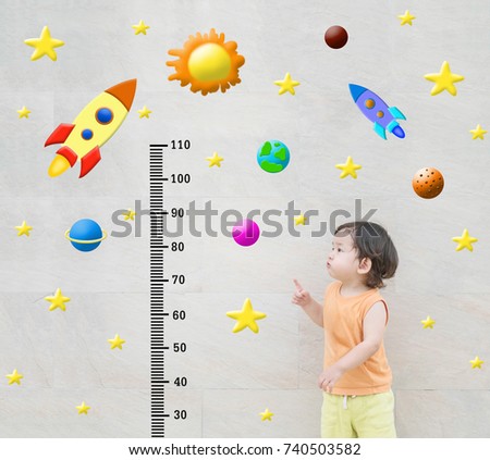 Closeup happy asian kid stand and point to scale of measure height with cute cartoon at the marble stone wall textured background in growth of kid concept