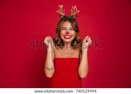 Portrait of an excited smiling girl wearing christmas deer costume while standing with eyes closed isolated over red background