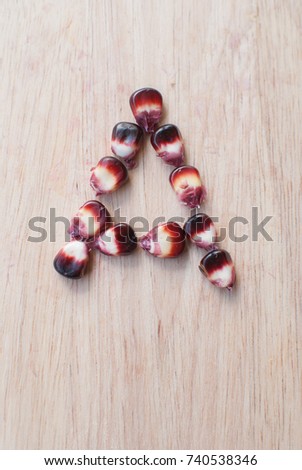 Alphabet "A" of Sweetcorn seeds on wood background