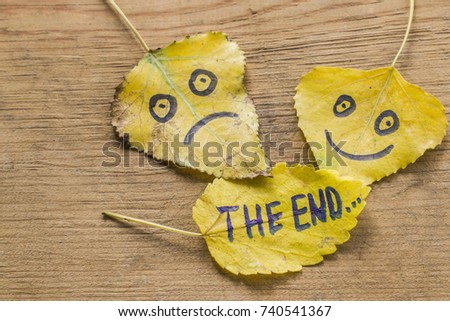 Yellow leaves with a picture of a happy and sad face and the inscription THE END on an old wooden background with cracks