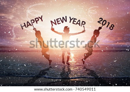 Happy New Year 2018 on children hand, silhouette children holding happy new year 2018 text and jumping up in seascape with sunset background