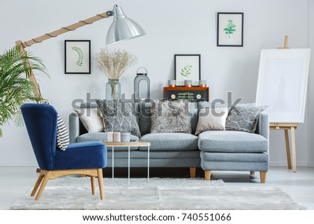 Trendy interior design with gray elegant sofa, navy blue armchair and patterned pillows
