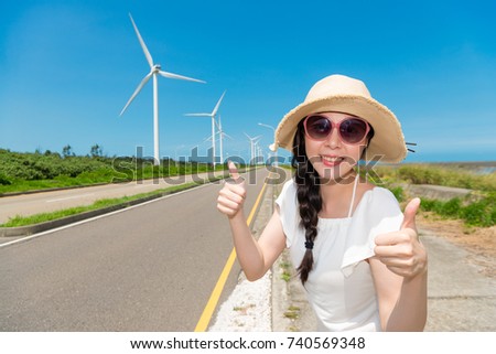 happy Asian woman makes a thumbs up to love and agree on travel with green windmill power for her holiday with great sunny weather