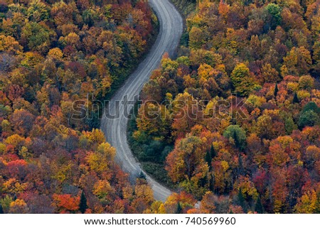 Scenic aerial view looking at a winging road in the middle of the colorful Laurentian forest during fall season in Quebec, Canada.