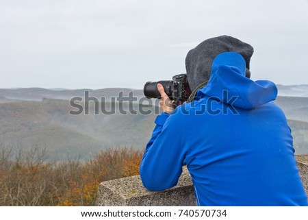A photographer takes a photo on a mountain in Wienerwald on a foggy gloomy autumn day.