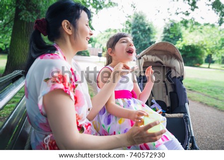 Portrait of young happy mother who sitting on bench outdoor and keeping on the laps beautiful daughter who is invalid and mother keeping cup of drink in hand
