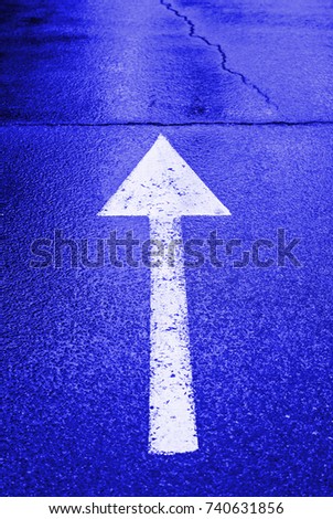 White arrow on the wet asphalt, detail of an arrow of direction, traffic signal