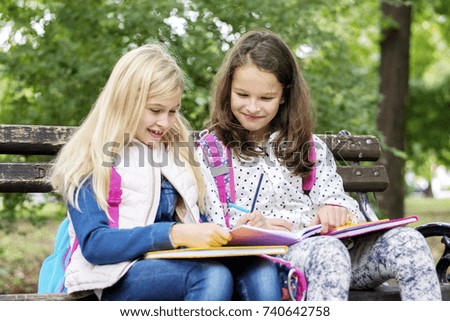 Two adorable little schoolgirls studying in a city park
