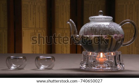 Beautiful warm picture of transparent teapot kettle with tasty green black tea on a table with candles. Glass kettle with blooming flower tea on wooden table. Stand with little candle. Chinese tea
