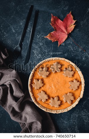 Homemade pumpkin pie decorated with cookies in shape of maple leaf on blackboard. Top view, vertical