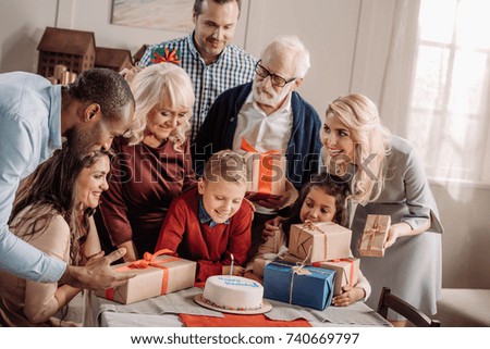 large family presenting cake and gifts to surprised little boy