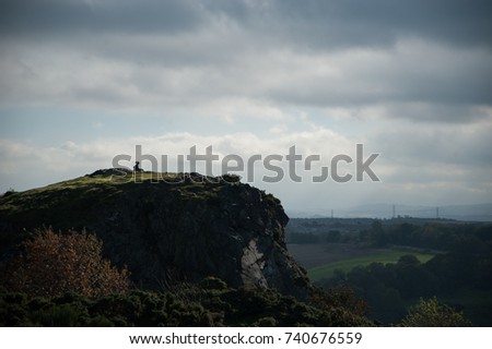 A silhouette of a women sitting on a giant cliff  with dramatic clouds