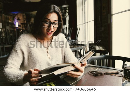 Surprised young woman looks at old photoalbums sitting in a cafe