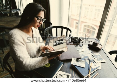 Charming young woman looks at old photoalbums sitting in a cafe