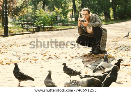 Woman takes a photo of pigeons standing in the park