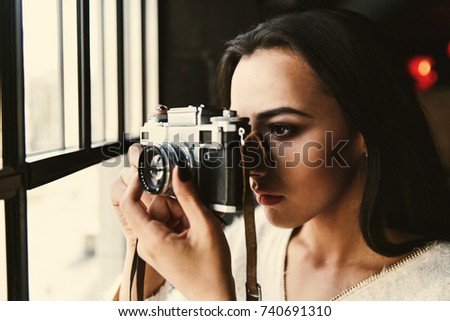 Girl takes a photo standing before a bright window