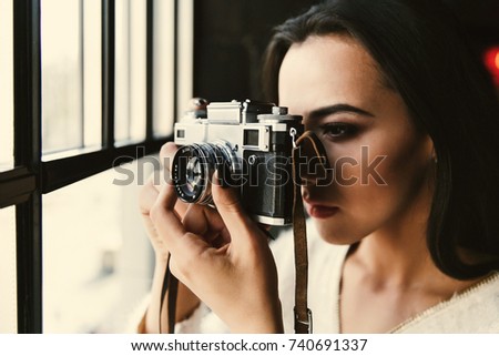 Girl takes a photo standing before a bright window