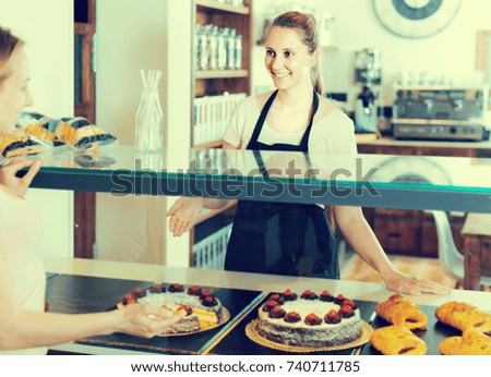 Bakery smiling spanish female worker with delicious pies and rolls on counter