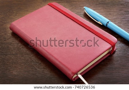Red leather notebook with pens on wooden table, selective focus for copy space.