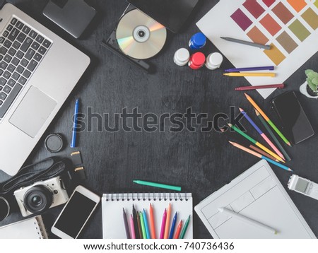 top view of graphic designer work space with graphic tablet, smartphone, sample color swatches, laptop and other accessories on black wooden background with copy space, creative designs concept