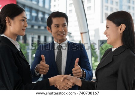 business man show thumb up and two business woman shaking hands and smile for demonstrating their agreement to sign agreement or contract between their firms, companies, enterprises. success concept