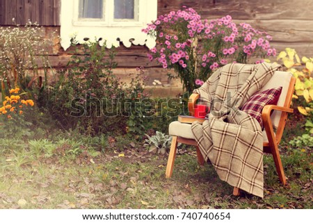 old chair with blanket, book and red mug stands in the garden near village house / comfortable place to rest