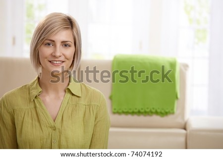 Portrait of attractive blonde woman smiling at home, sofa in background.