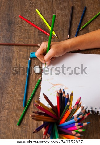 girl hand drawing, paper and colorful pencils on wooden table