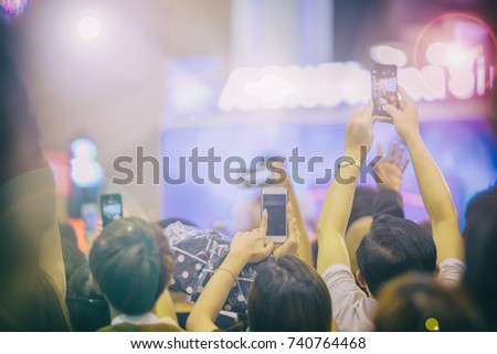 Asian  women holding smart phone and tapping screen for taking pictures on Crowd at concert stage lights,blurry background
