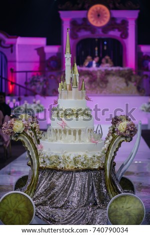 Wedding cake made like a fairy tale castle stands on the table with silver cloth and flowers