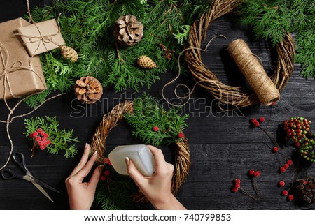 Top view of female hands make a Christmas wreath. Packed gifts and scrolls, spruce branches and tools on wooden table.