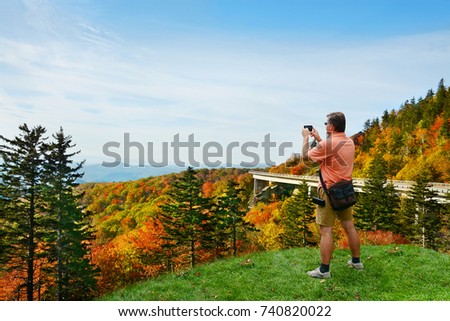 Man standing on top of the mountain taking photos ,looking at beautiful autumn mountains landscape foliage. Linn Cove Viaduct,  Blue Ridge Parkway. Copy space. North Carolina, USA.