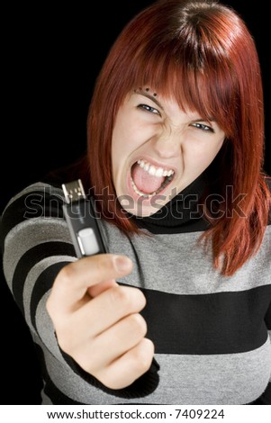 Beautiful redhead girl holding an usb memory stick or flash drive at the camera with an angry expression. Studio shot.