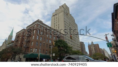 Establishing shot wide view of busy Manhattan intersection. Apartment, office buildings line street, storefront awnings on sidewalk level. Cars pass through traffic light on road, pedestrian crosswalk