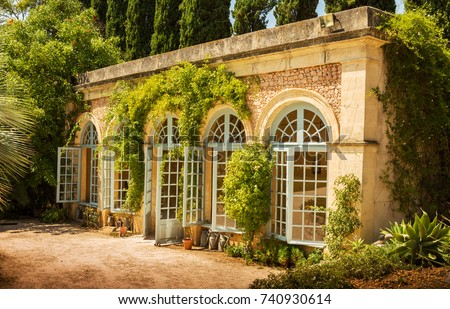 Garden plants conservatory (orangery) building - architecture. Stone elevation with blue windows and climbing plants. Royalty-Free Stock Photo #740930614