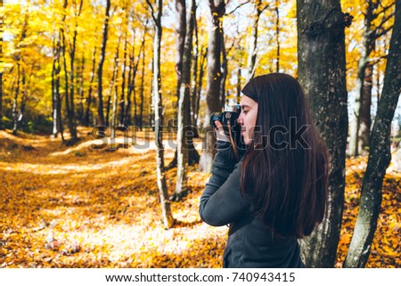 youang pretty woman taking picture in yellow forest at old retro camera