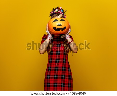 Colorful halloween. young woman in Mexican style halloween costume isolated on yellow holding jack-o-lantern pumpkin in the front of face