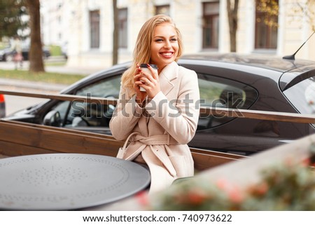 Beautiful happy woman in a trendy coat holds a cup of coffee and enjoys the moment outdoors