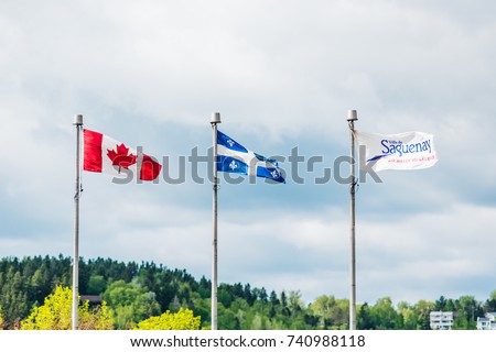 Flag poles with Quebec, Canadian and Saguenay symbols against sky in wind