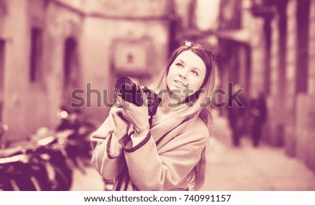 Young positive cheerful woman with camera looking curious and taking a pictures outdoors
