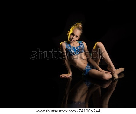 A young girl athlete gymnast performs acrobatic elements on a black background in a yellow scenic light.