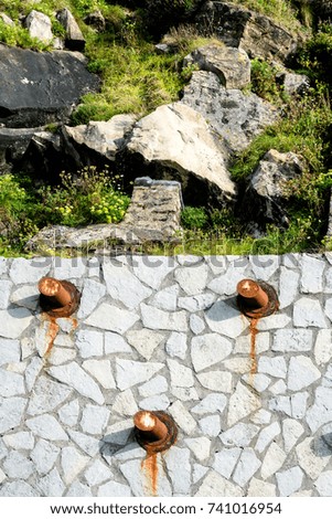 Few rusty anchoring in stone wall with background of rocks and grass on top.