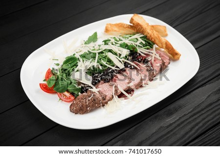 Grilled duck meat and spinach leaves in white plate on black wood background