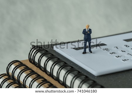 Miniature people figure businessman standing on white calculator and notebook as business financial concept.