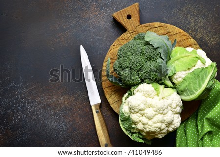 Raw broccoli and cauliflower on a oak cutting board over dark brown slate,stone or concrete background.Top view with copy space.
