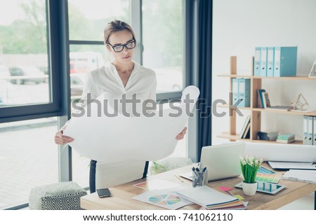 Creative brown haired serious focused concentrated lady is doing paper work, nice interior, huge windows, shelves with folders, perfect work station. Remodeling, visual art design, tone, web