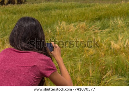 A young woman taking a picture with her smartphone on a wild grass crop.
