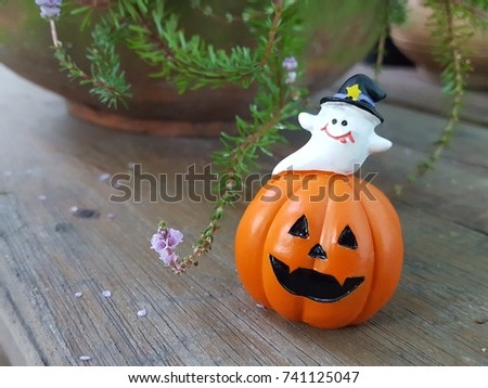 Halloween scary pumpkin and little ghost with a smile in flowerpot on the old wood table. Autumn forest. Holiday decoration. (Focus selected)