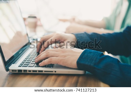 Young hipster worker typing on laptop keyboard while working in office with coworker. Freelancer activity and lifestyle concept with photo filter effect