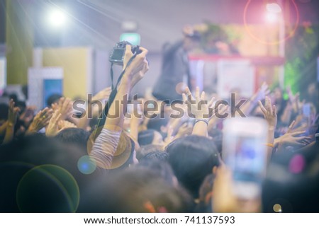 Asian  women holding camera for taking pictures on Crowd at concert stage lights,blurry background
